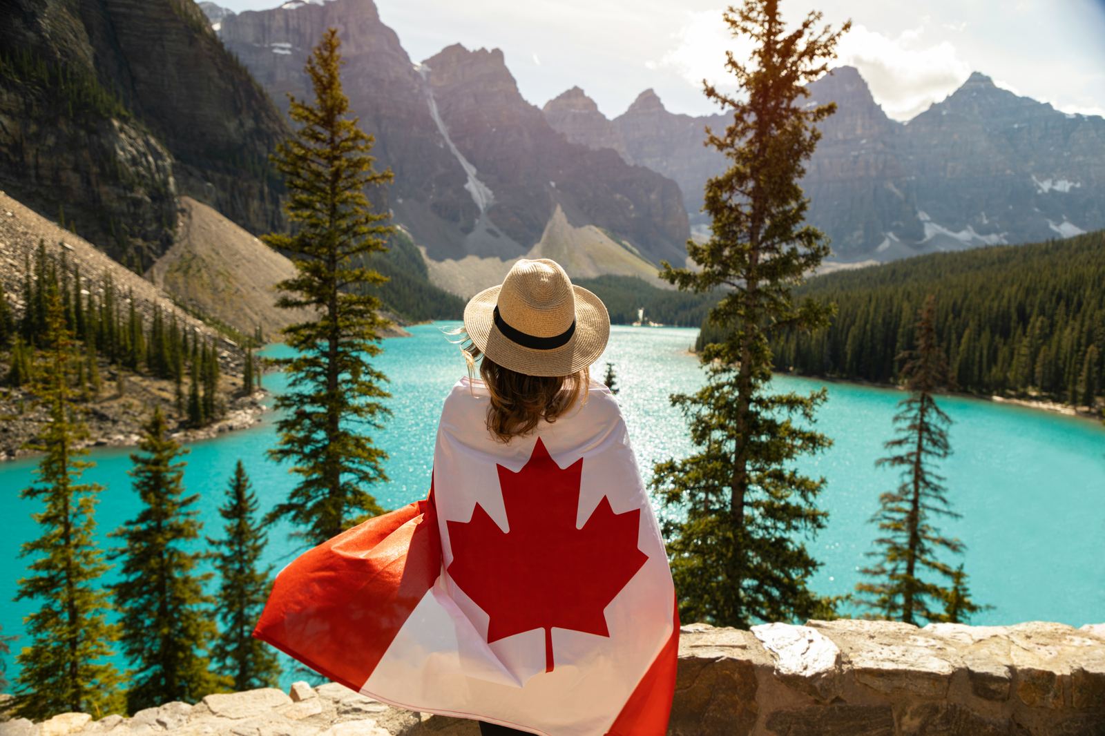 Person wrapped in a Canadian flag overlooking a mountain lake