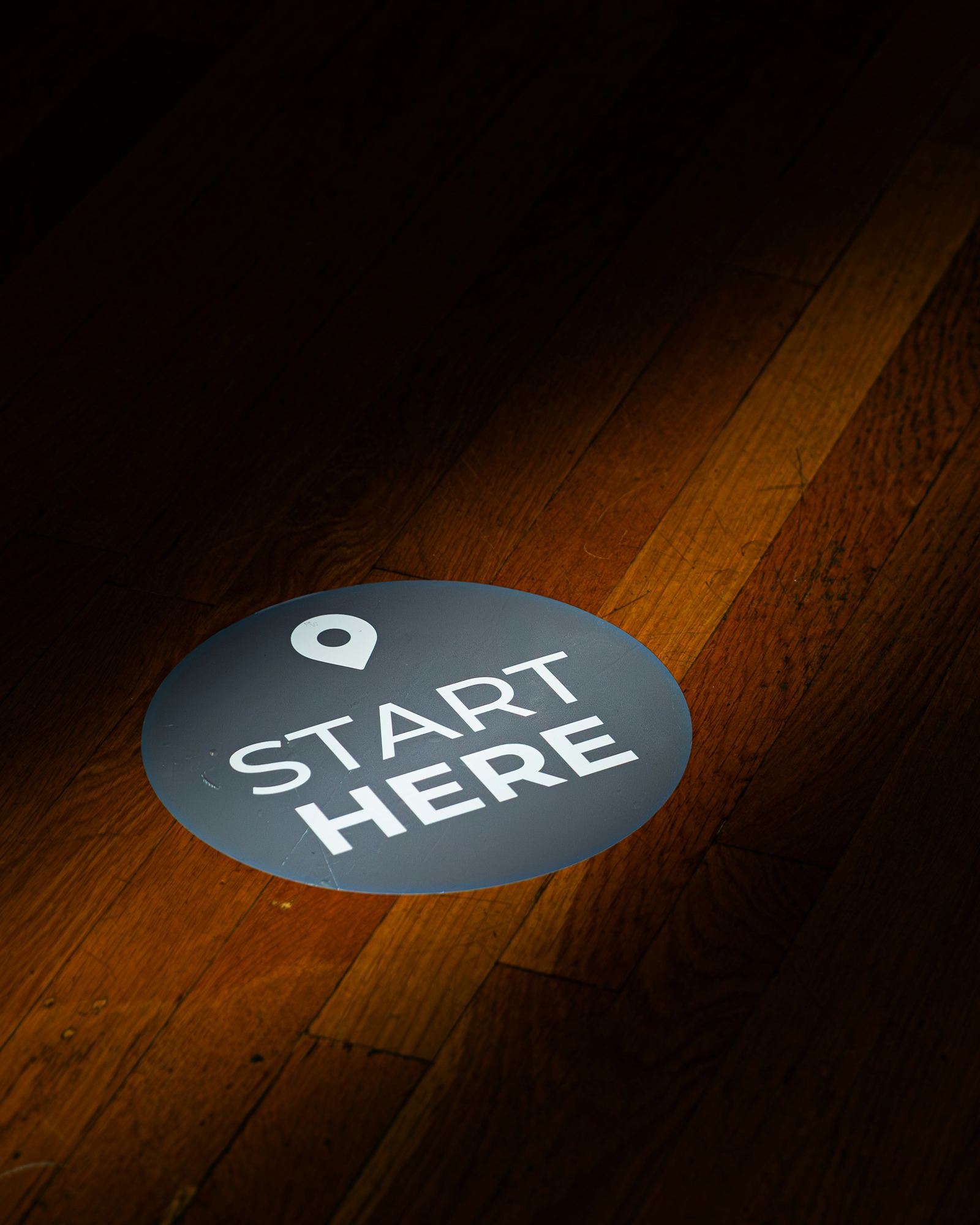 A 'Start Here' floor marker spotlighted on a wooden floor